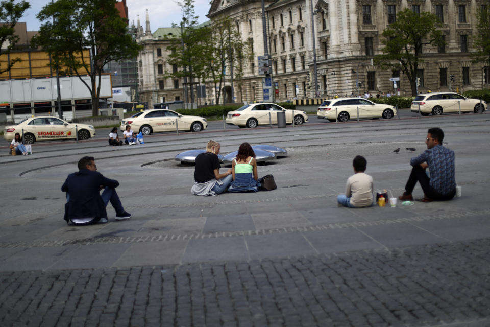 People sit around the closed fountain at the 'Karlsplatz' square during the lockdown due to the coronavirus outbreak downtown in Munich, Germany, Saturday, May 9, 2020. Due to the coronavirus the economy worldwide expects heavy losses. (AP Photo/Matthias Schrader)