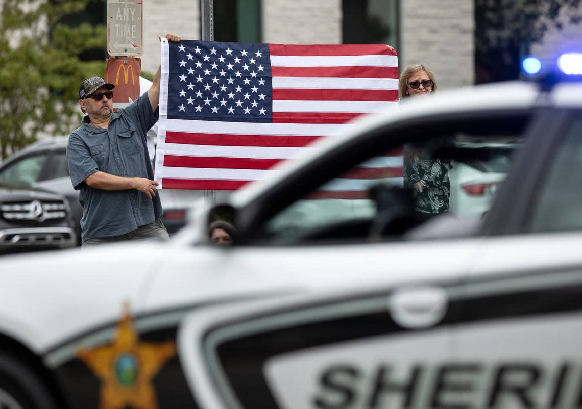 Raleigh residents Ray Johnson and Wendy Thornton hold an American flag as law enforcement drives along Glenwood Avenue following the funeral for Wake County Deputy Ned Byrd on Friday, Aug. 19, 2022, in Raleigh, N.C. Byrd was found dead with multiple gunshot wounds early Friday morning, Aug. 12 in southeastern Wake County.