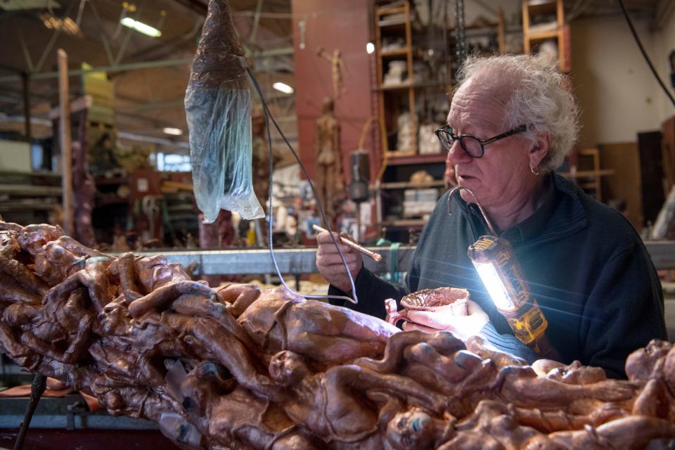 A man closely examines the Pillar of Shame sculpture, which turned on its side, with a bright light.