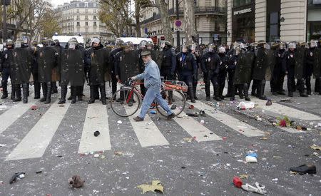 A man with a bicycle walks past CRS riot policemen after clashes with demonstrators at the Place de la Republique after the cancellation of a planned climate march following shootings in the French capital, ahead of the World Climate Change Conference 2015 (COP21), in Paris, France, November 29, 2015. REUTERS/Eric Gaillard