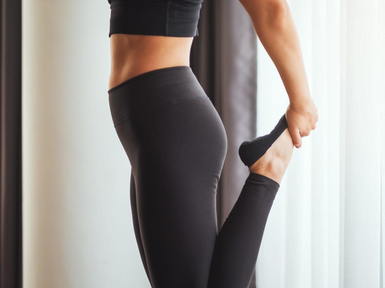 A woman wearing activewear sports bra and leggings/yoga pants, stretching, pictures from the knee to mid-torso