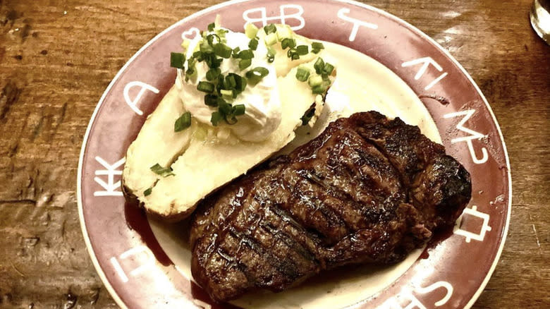 Baked potato with sour cream and chives beside steak