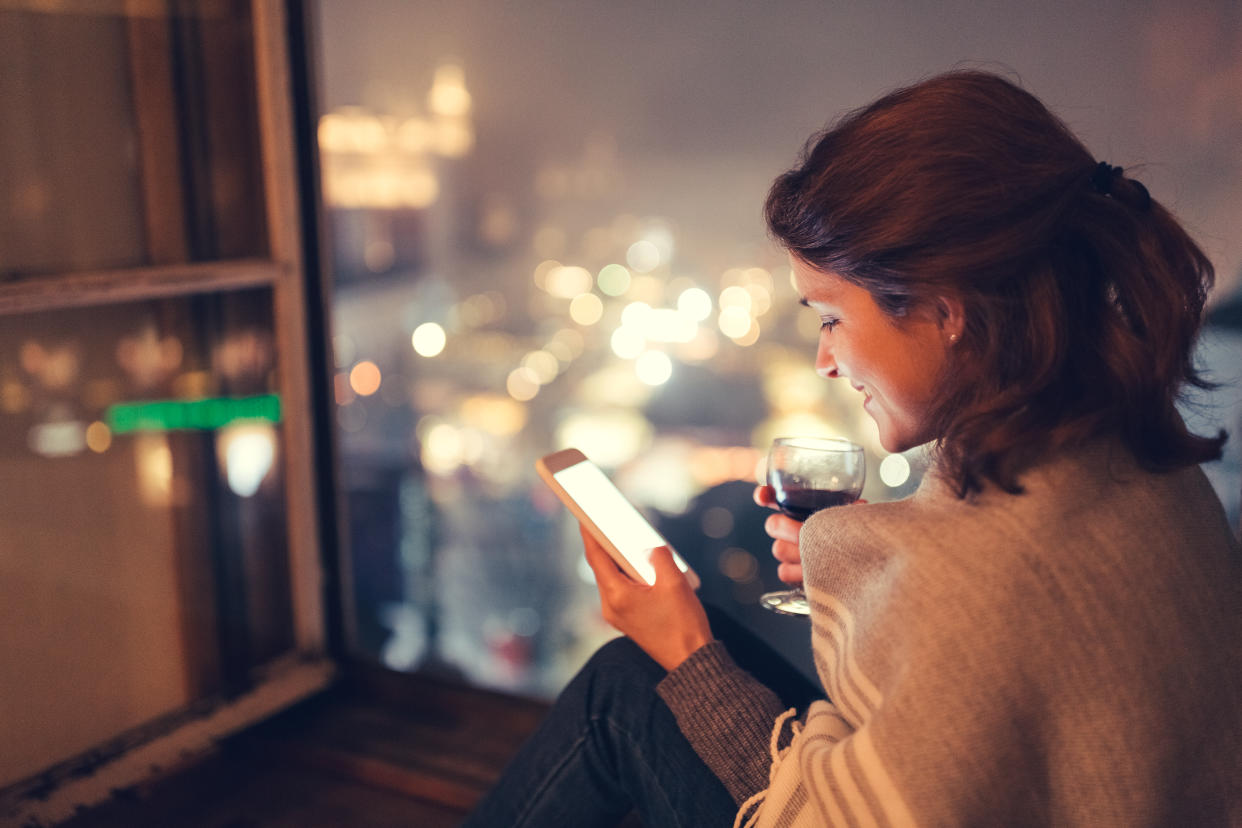 Woman on the window drinking wine and text messaging