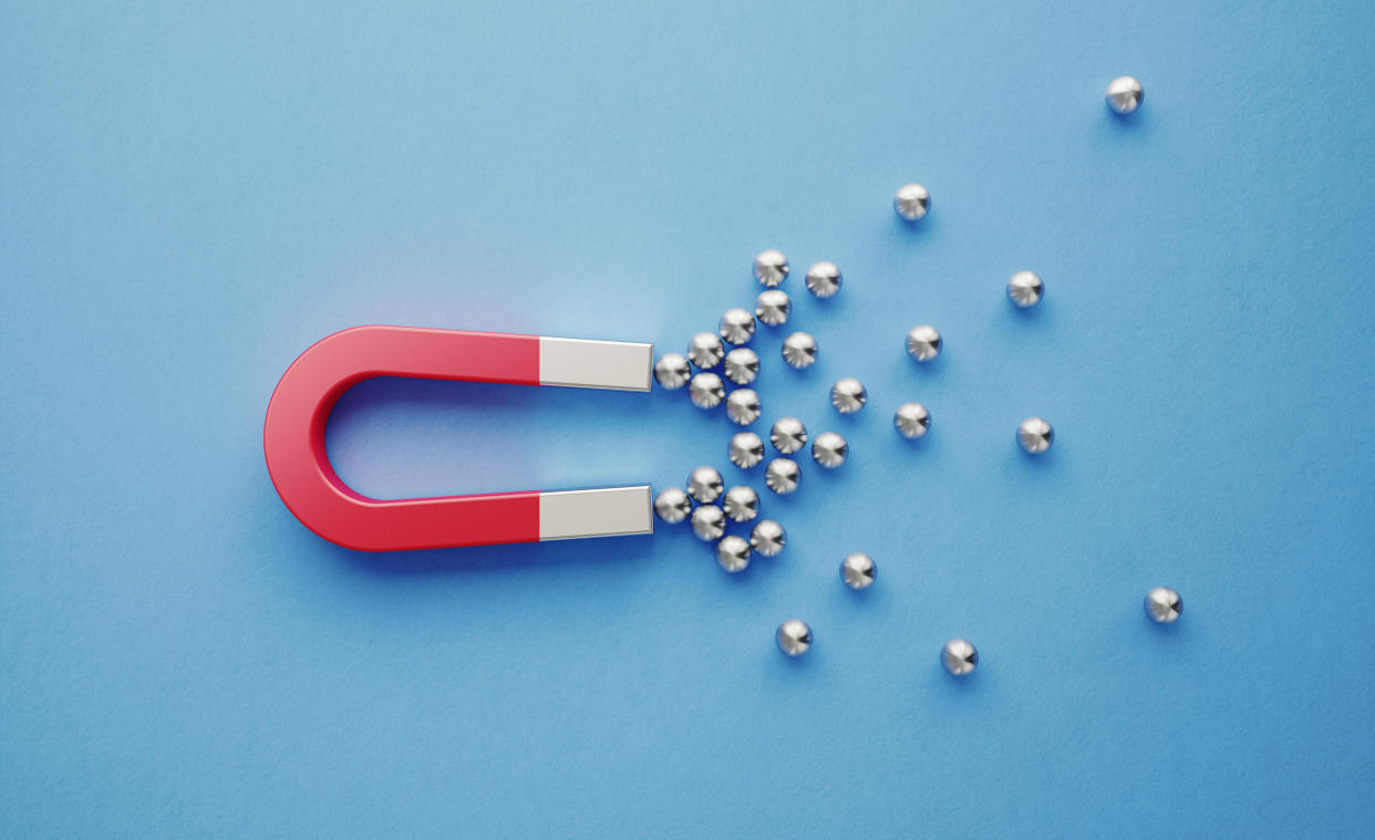 Silver spheres gravitated towards a red magnet on blue background. Horizontal composition with copy space. Digital marketing concept.