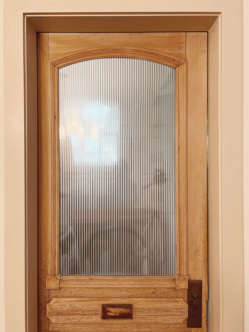 Vintage door in a natural wood tone, featuring an arched glass pane that looks like reeded glass