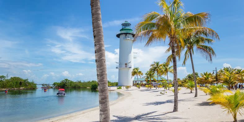 scenic view of a tropical white sand beach on the caribbean coastline of belize, a big lighthouse is in the background and boats are visible in the water