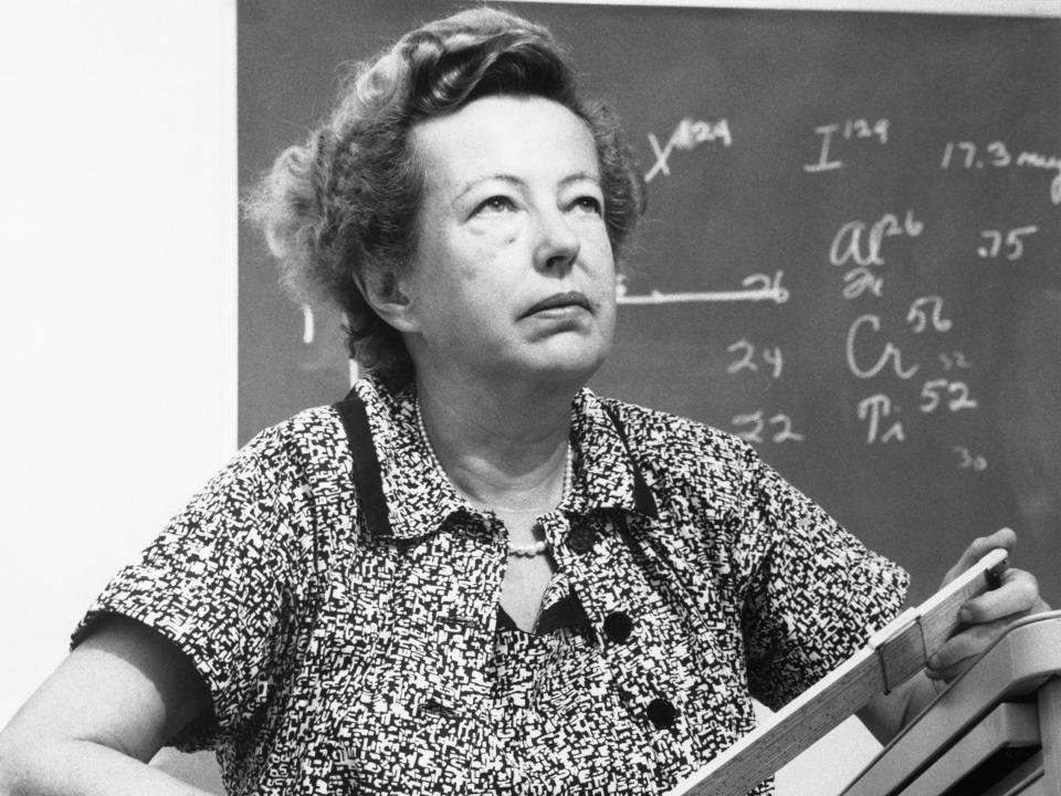 A portrait of Maria Goeppert Mayer standing in front of a chalkboard.