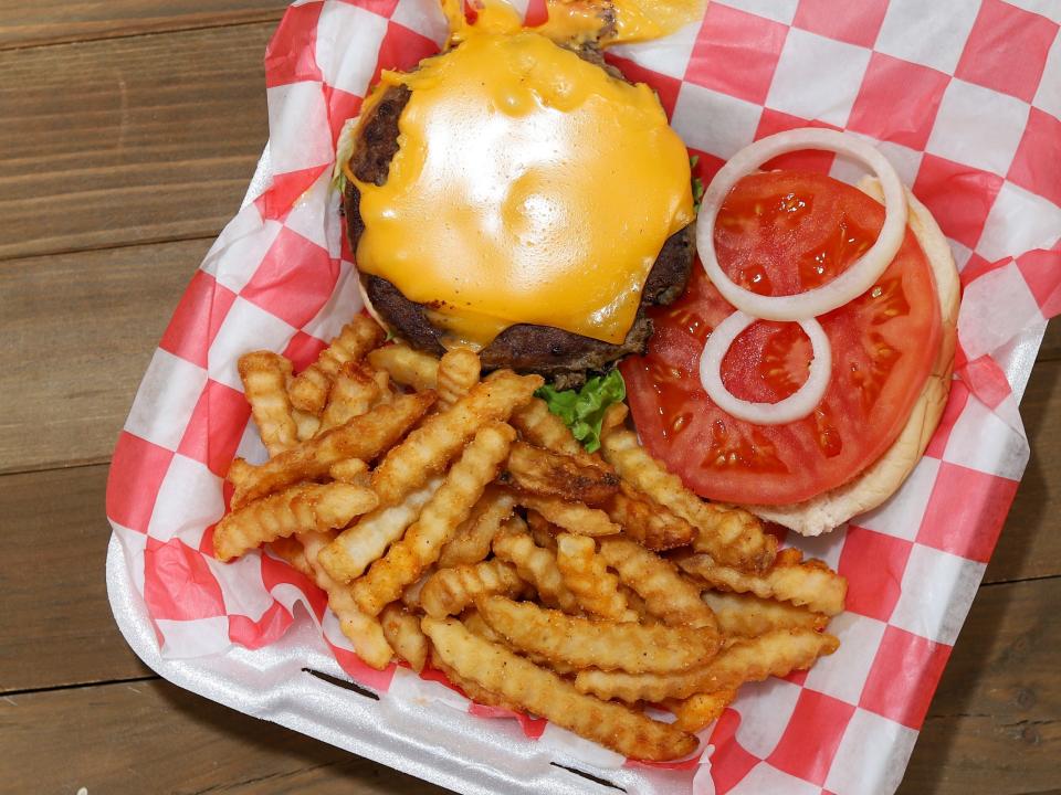 french fries and an open face cheeseburger on a checkered sheet of paper in a takeout box