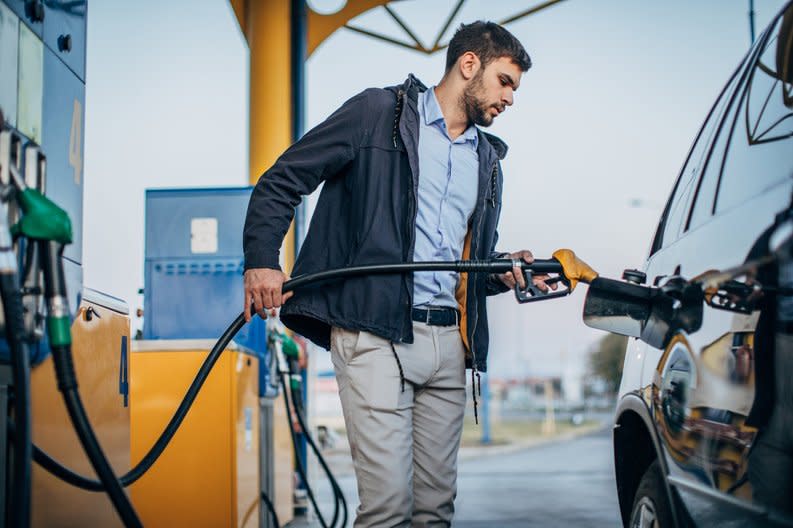 A person standing next to their car pumping gas at a gas station.