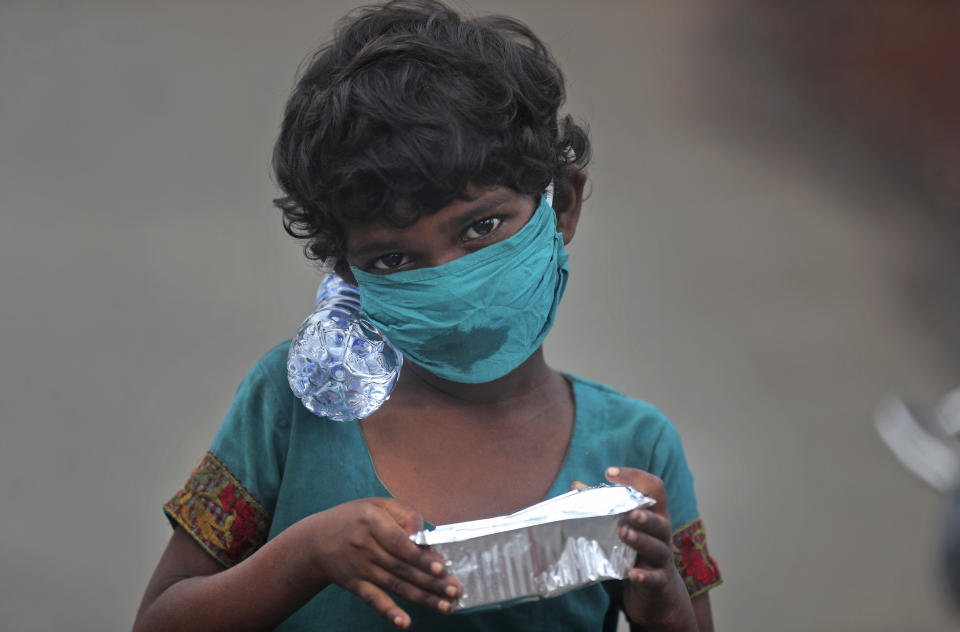 A girl wearing a face mask walks with a bottle of drinking water and a food packet that she received from a food distribution site in Mumbai, India, Saturday, June 20, 2020. India is the fourth hardest-hit country by the COVID-19 pandemic in the world after the U.S., Russia and Brazil. (AP Photo/Rafiq Maqbool)