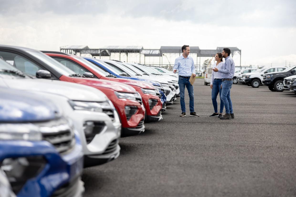 Happy salesman showing cars to a couple at the dealership - car ownership concepts