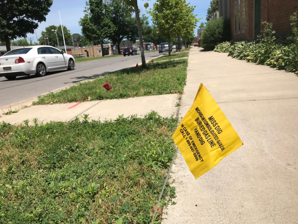 A MISS DIG warning flag — yellow for natural gas — marks a buried pipe under a sidewalk on Mack Avenue in Grosse Pointe Farms on June 30, 2019.