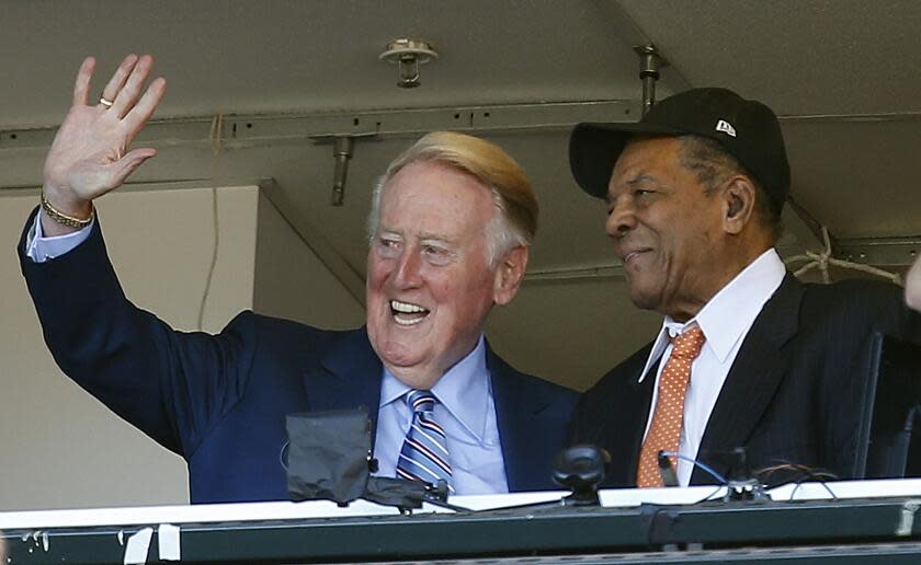 FILE - In this Oct. 2, 2016, file photo, Los Angeles Dodgers announcer Vin Scully waves to fans alongside Hall of Famer baseball player Willie Mays during the fourth inning of a baseball game between the San Francisco Giants and the Los Angeles Dodgers in San Francisco. On Monday, April 3, 2017, the Dodgers will play their first opening day since 1950 without Scully calling their games. He won't be in the stands. He won't make a point of watching on TV, either. (AP Photo/Tony Avelar, File)