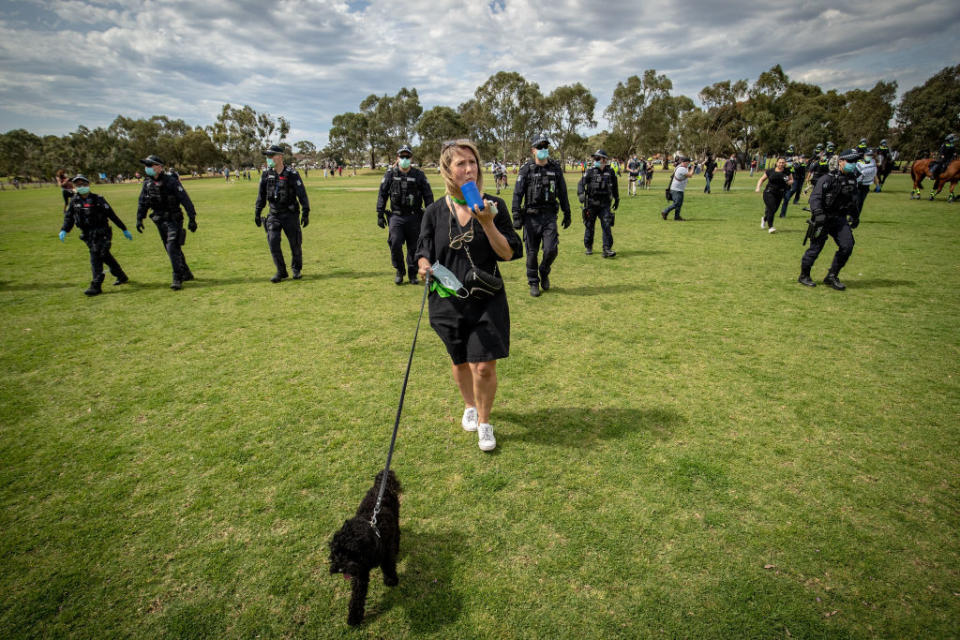 Woman walks her dog while wearing a mask as a group of police officers walk behind her in Melbourne. Source: Getty