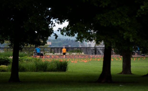 People pause to look at orange flags, representing children who died while attending residential schools in Canada, placed in the grass at Major's Hill Park in Ottawa, on Canada Day 2021. (Justin Tang/The Canadian Press - image credit)