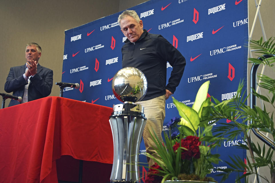 Duquesne University men's basketball coach Keith Dambrot, center, glances at the Atlantic 10 Championship trophy at the end of a gathering in Pittsburgh celebrating Duquesne earning a berth in the NCAA Men's Basketball Tournament for the first time since 1977 Monday, March 18, 2024. Dambrot announced that he is retiring after his team's NCAA tournament run. (AP Photo/Gene J. Puskar)