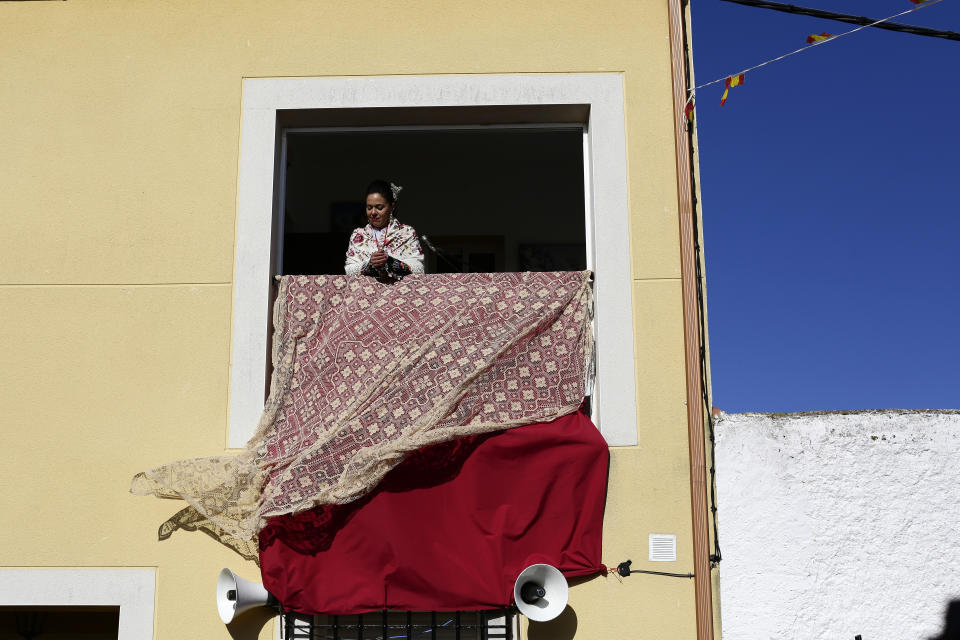 In this photo taken on Monday, Jan. 20, 2020, a woman dressed in traditional costume watches from a balcony the traditional "Carantonas" festival in Acehuche, Spain. The Carantonas involves men pulling on animal hides that make them look like Chewbacca. At the Carantoñas festival in Acehuche, men are helped to pull on hairy, bulky costumes and scary masks before they walk down streets of whitewashed houses looking like wild beasts ("carantoñas"). Women parade in colorful embroidered shawls and skirts as music plays. (AP Photo/Manu Fernandez)