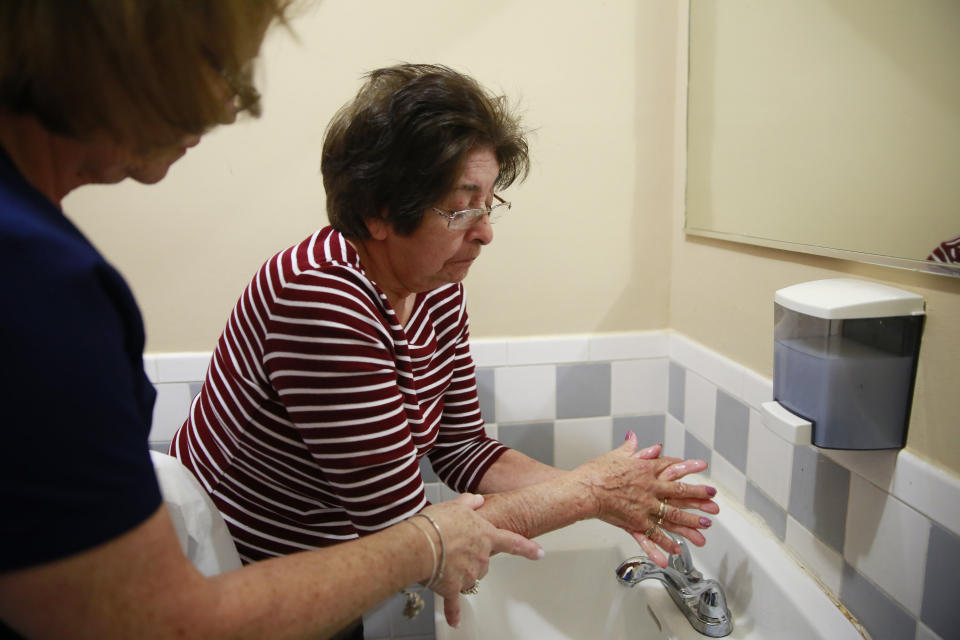 In this March 4, 2020, photo, Maria Casal Hernandez, RN., left, helps Maria Castro wash her hands at Little Havana Activities and Nutrition Centers of Dade County, Inc., in Miami. The new coronavirus is posing a special challenge for nursing homes and other facilities that provide care for the elderly. (AP Photo/Brynn Anderson)