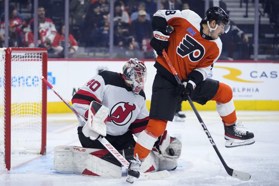 New Jersey Devils' Akira Schmid, left, catches a shot as Philadelphia Flyers' Morgan Frost screens during the second period of an NHL hockey game, Thursday, Nov. 30, 2023, in Philadelphia. (AP Photo/Matt Slocum)