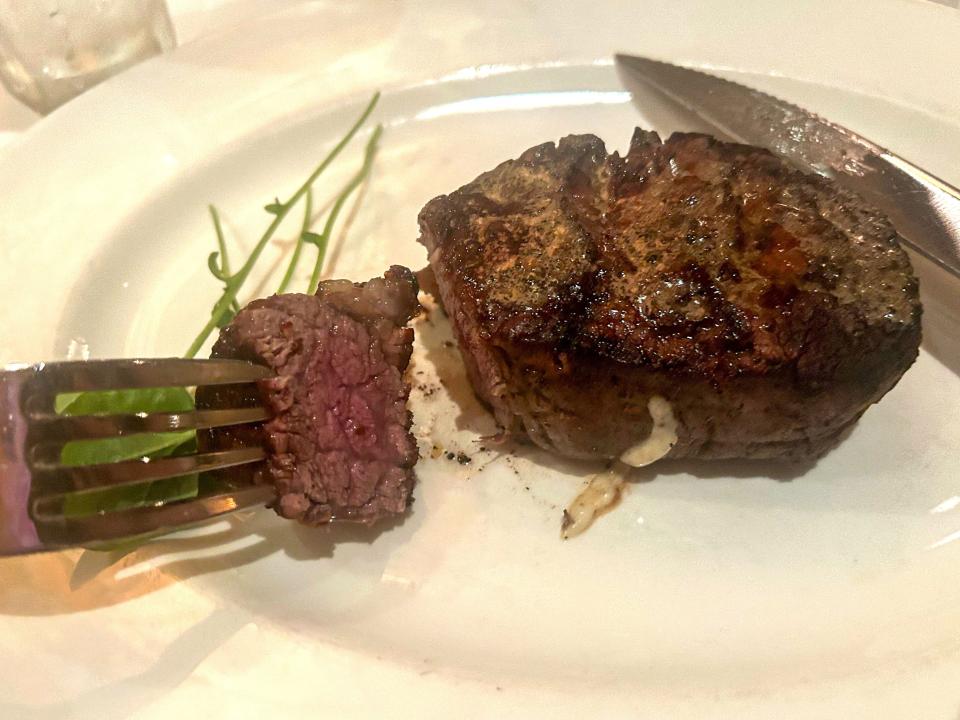 A piece of steak on a fork. The rest of the steak and a knife are on a white plate.