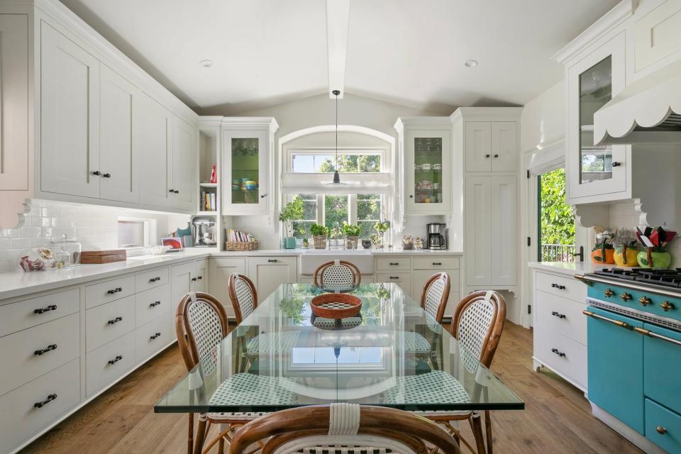 A kitchen with white cabinets, a glass table, and a blue oven.