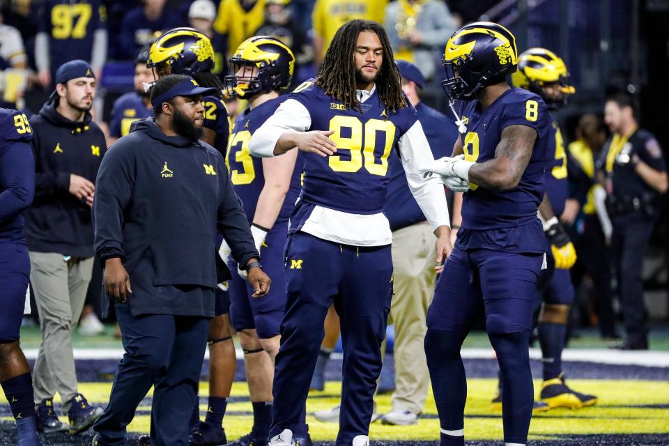 Michigan linebacker Mike Morris (90) shakes hands with linebacker Derrick Moore (8) warms up before the Big Ten  championship game against Purdue at Lucas Oil Stadium in Indianapolis on Saturday, Dec. 3, 2022.