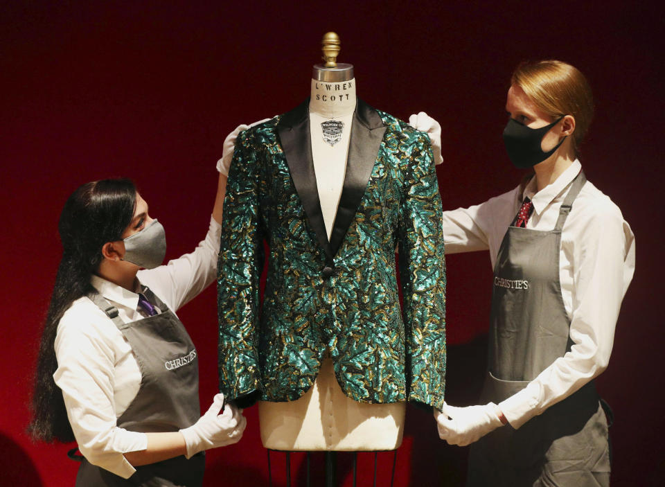 Gallery assistants handle the oak leaf 'Glamouflage' jacket made for Mick Jagger, amongst other items on display at Christie's, from the archive of fashion designer L'Wren Scott before it is offered at auction, in London, Thursday June 10, 2021. (Jonathan Brady/PA via AP)