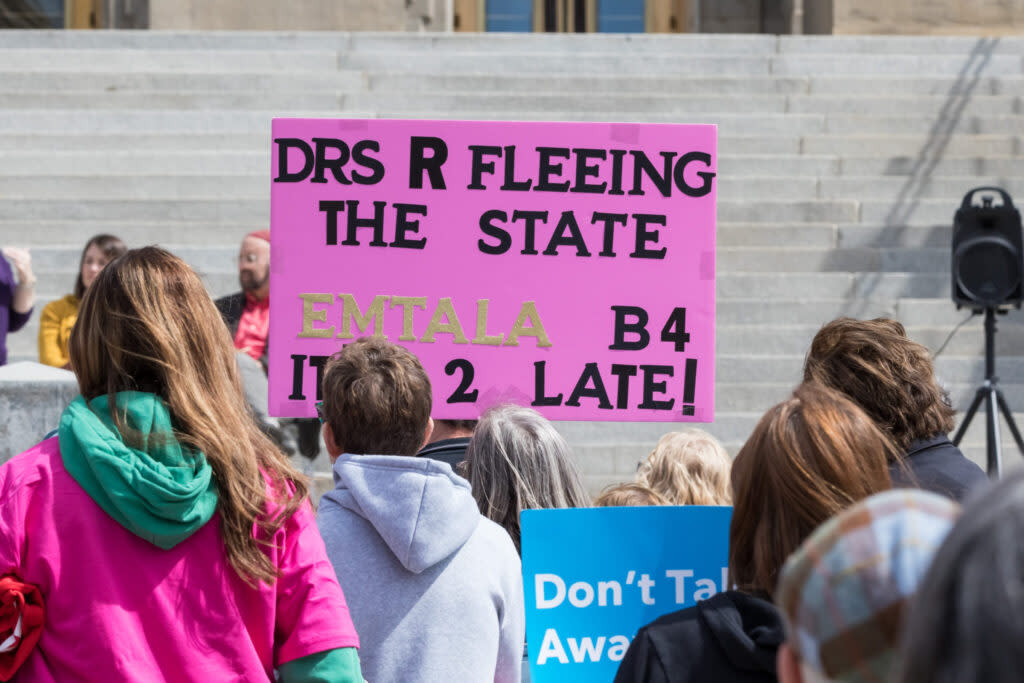 A person holding a sign saying "Doctors are fleeing the state EMTALA before it's too late."