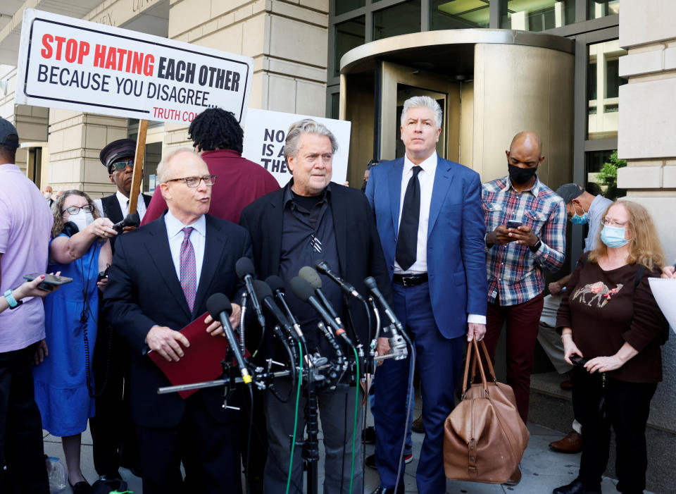 Bannon, outside the courthouse flanked by his lawyers, one of whom is speaking, with a demonstrator in a surgical mask holding a banner behind him saying: Stop Hating Each Other Because You Disagree, Truth.com.