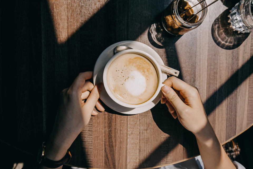 Top view of woman sitting by the window in coffee shop enjoying the warmth of sunlight and drinking coffee