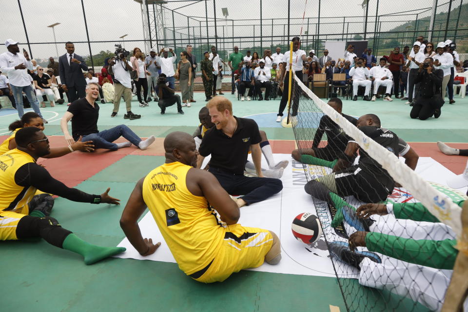 Prince Harry sits on the ground with others at a volleyball event, engaging with the community