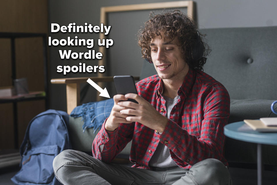 A guy sitting cross-legged on the floor looking at his phone with the caption "Definitely looking up Wordle spoilers"