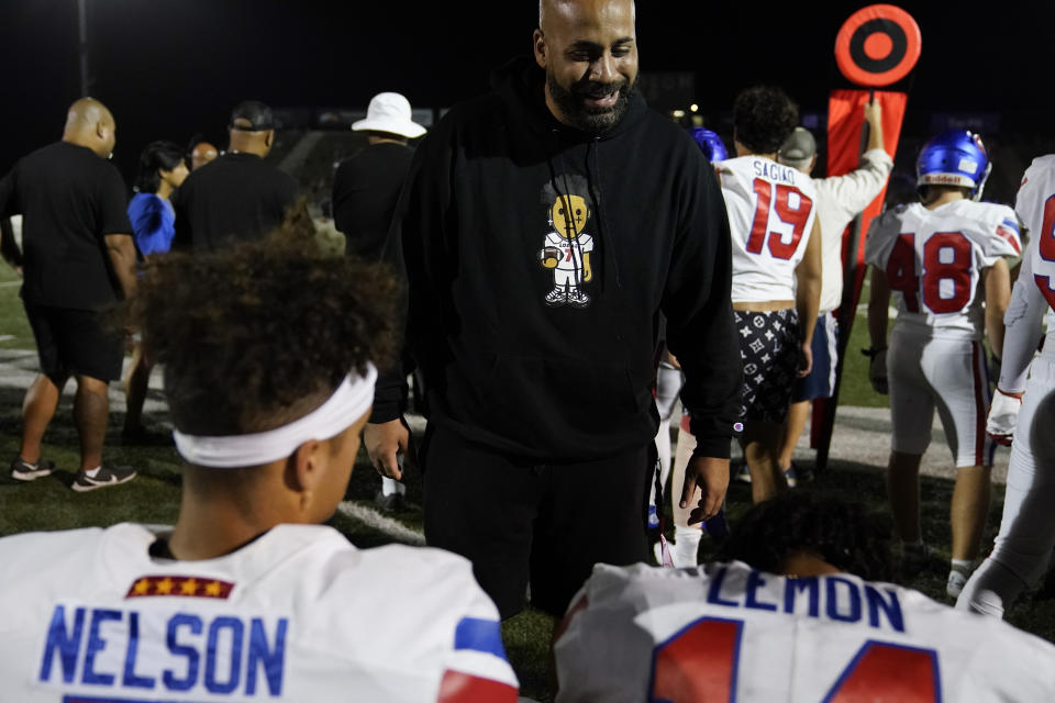 Eric Nelson, center, talks with his son, Los Alamitos High School quarterback Malachi Nelson, left, and wide receiver Makai Lemon on the sideline during a high school football game against Newport Harbor High School on Friday, Sept. 30, 2022, in Newport Beach, Calif. (AP Photo/Ashley Landis)