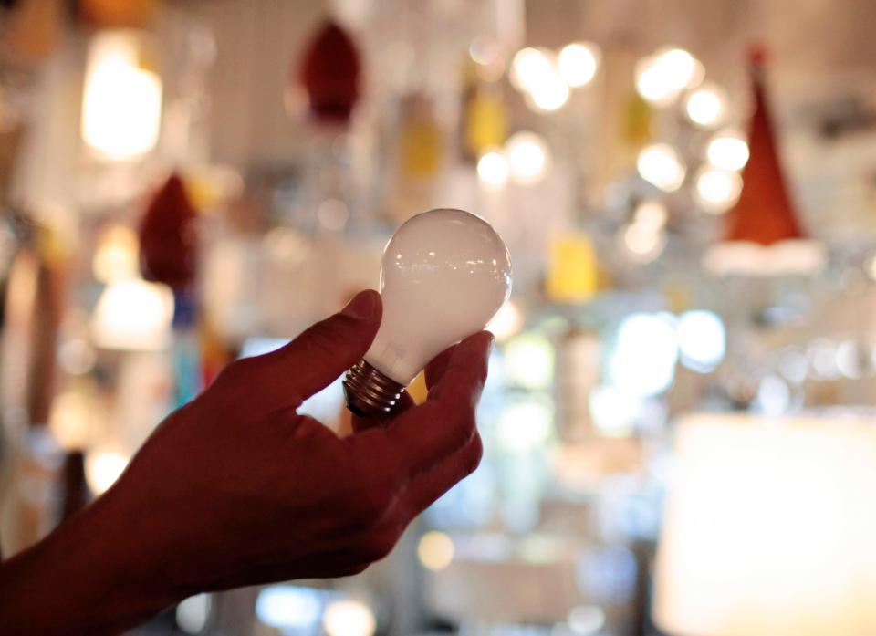 a hand holds an incandescent light bulb in a lighting store