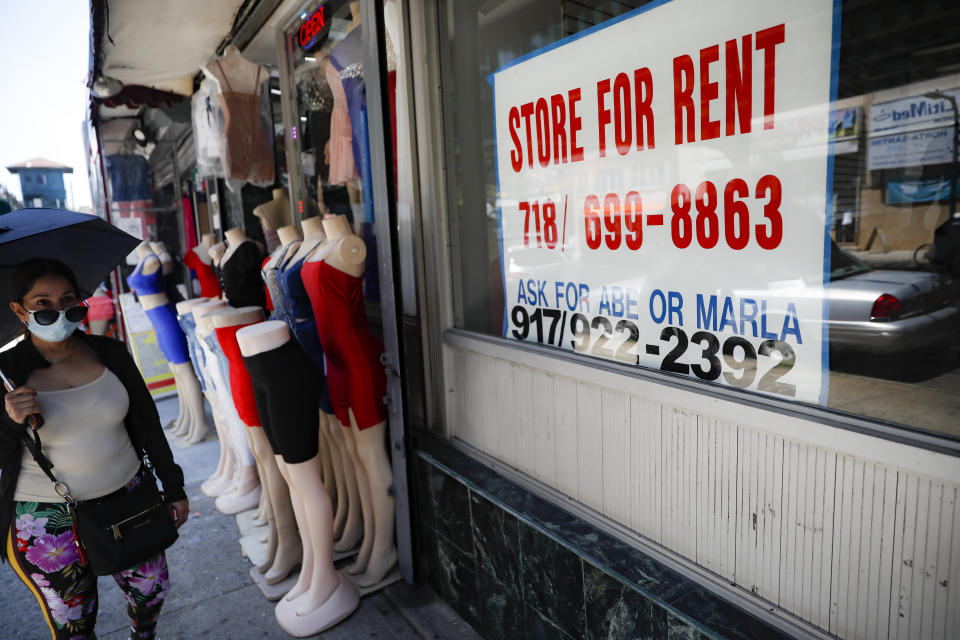 Pedestrians pass a storefront for rent as a neighboring business sells clothing during the COVID-19 pandemic, Tuesday, June 23, 2020, in the Corona neighborhood of the Queens borough of New York. (AP Photo/John Minchillo)