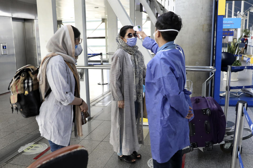 A health worker, right, checks temperature of passengers to help prevent the spread of the coronavirus upon arrival at the departure terminal of Tehran's Imam Khomeini airport, Iran, Friday, July 17, 2020. The first Emirates flight arrived in Iran after nearly 5 months of suspension of the most airliners flights to the country due to the coronavirus outbreak, as Iranian officials at the airport say they are doing everything possible to ensure passengers are not infected, and isolate those with symptoms. (AP Photo/Vahid Salemi)