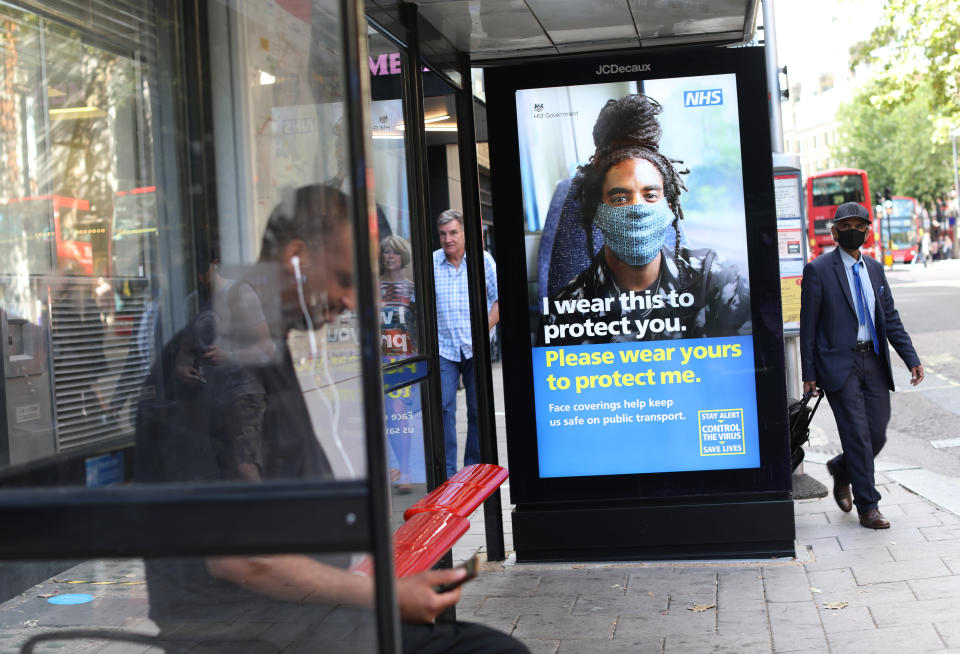 A man wearing face covering walks pass a screen on a bus stop in London displaying a NHS notice telling travellers to wear face covering for their safety on public transport, as face coverings becomes compulsory on public transport in England. Picture date: Friday August 7, 2020.