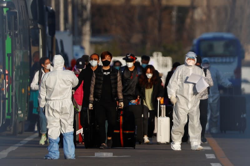 Staff in protective suits accompany passengers outside a centralized facility for screening and registration near the Beijing Capital International Airport in Beijing as the country is hit by an outbreak of the novel coronavirus