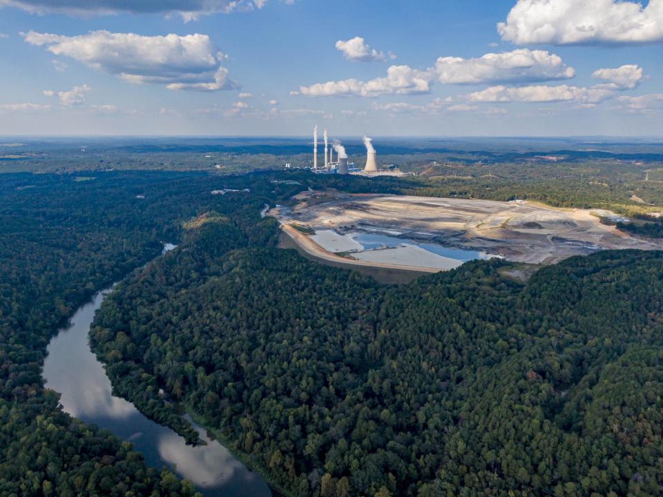 An aerial view of a blue-tinted coal ash pond, with a power plant in the background and woods and a river in the foreground.