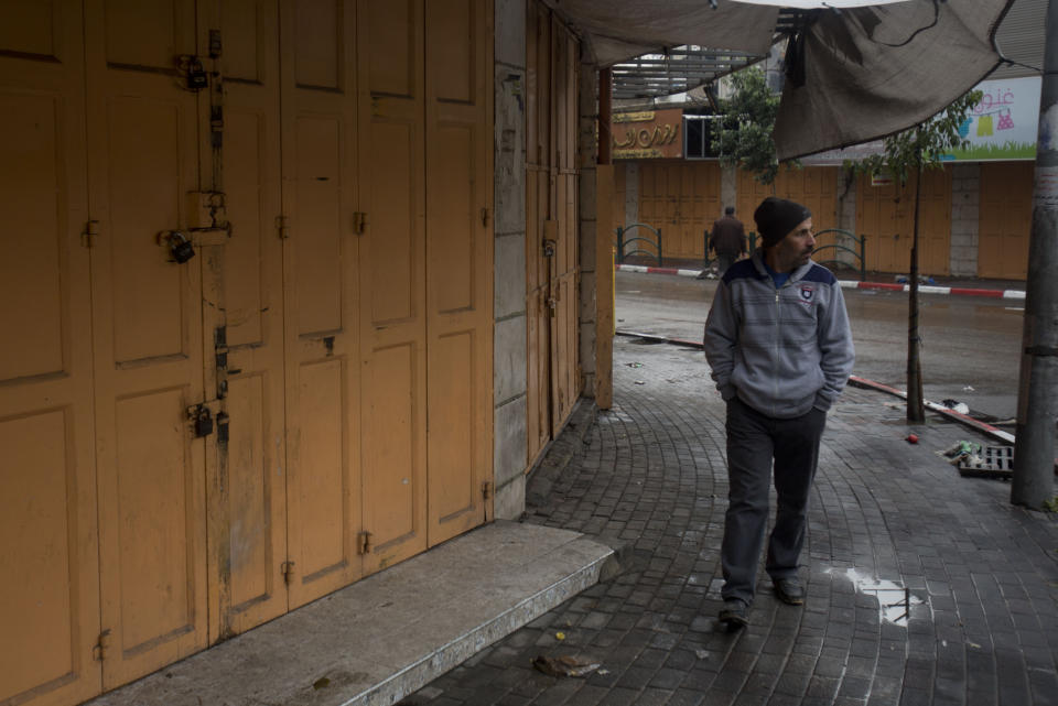 A Palestinian man walks near closed shops during a general strike in the West Bank city of Hebron, Monday, Dec. 9, 2019. Palestinian residents held a general strike to protest an Israeli plan to build a new Jewish neighborhood in the heart of the West Bank's largest city. (AP Photo/Majdi Mohammed)