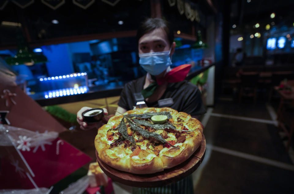 A staff member shows a pizza topped with a cannabis leaf at a restaurant in Bangkok, Thailand on Nov. 24, 2021. The Pizza Company, a Thai major fast food chain, has been promoting its "Crazy Happy Pizza" this month, an under-the-radar product topped with a cannabis leaf. It’s legal but won’t get you high. (AP Photo/Sakchai Lalit)