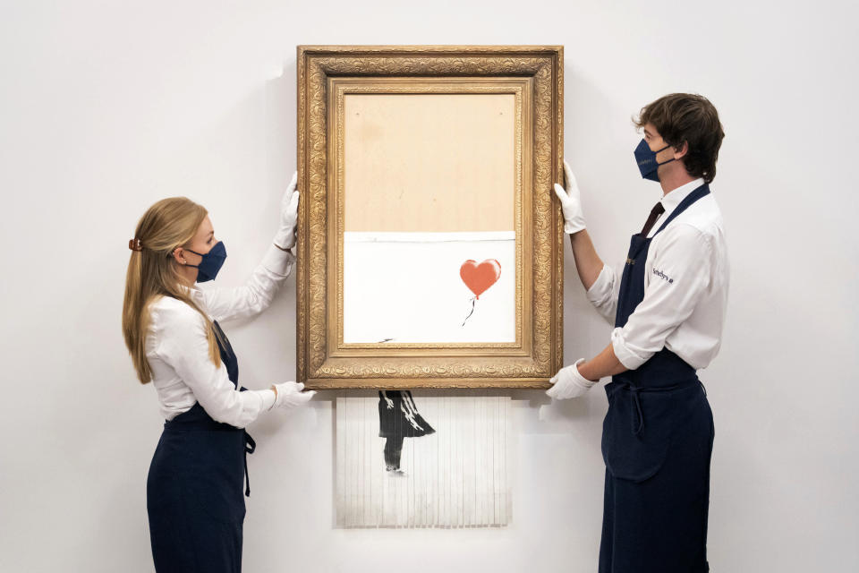 ARCHIVO - En esta foto del 3 de septiembre de 2021, manipuladores de arte sostienen "Love is in the Bin" de Banksy en la casa de subastas Sotheby's en Londres. La obra, que se autodestruyó de manera sensacional justo después de venderse por 1,4 millones de dólares, se ofrece de nuevo en subasta el jueves 14 de octubre con un precio de venta estimado en 4 a 6 millones de libras esterlinas (5,5 a 8,3 millones de dólares). (Dominic Lipinski/PA vía AP)