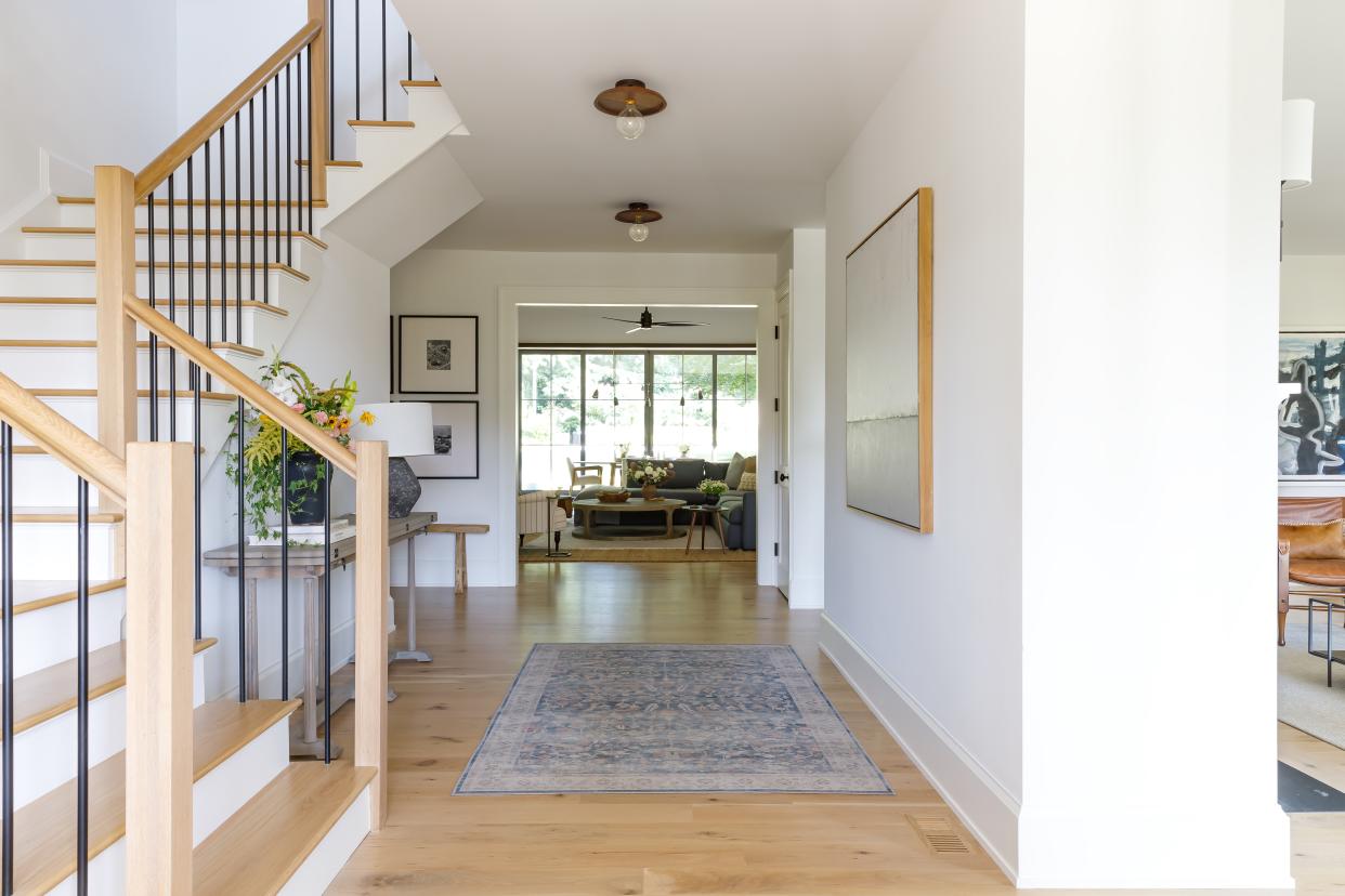  Bright entryway with staircase, console table and patterned rug. 