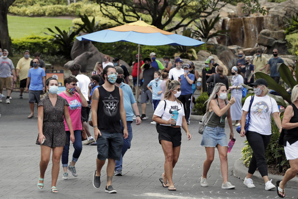 Guests wearing masks stroll through SeaWorld as it reopened with new safety measures in place Thursday, June 11, 2020, in Orlando, Fla. The park had been closed since mid-March to stop the spread of the new coronavirus. (AP Photo/John Raoux)