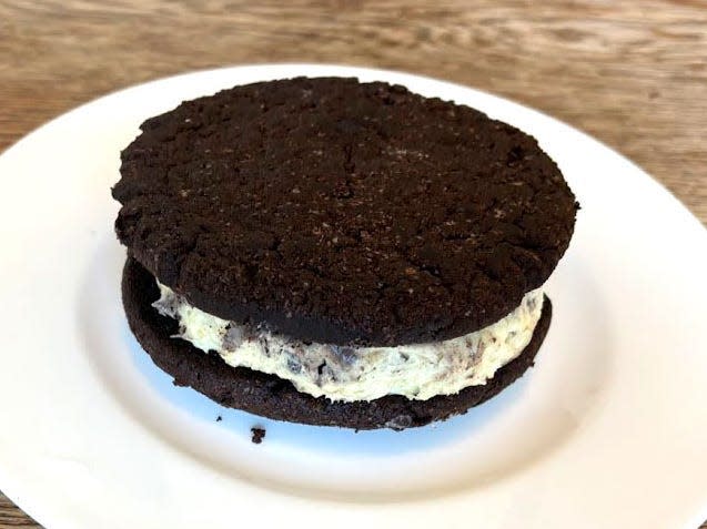 Two chocolate cookies with white frosting in between. The dessert is on a white plate.