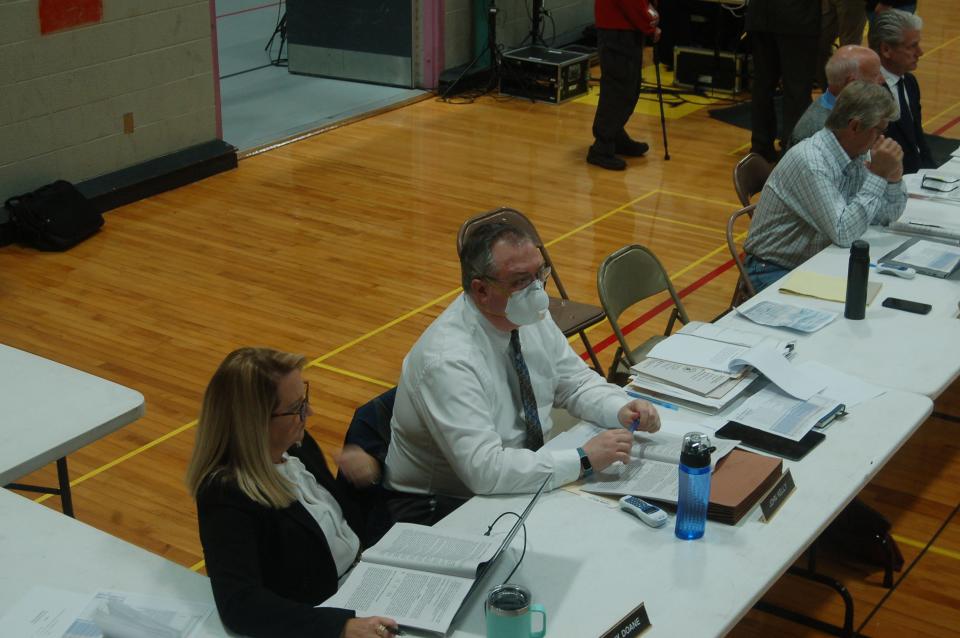 Orleans Town Administrator John Kelly, in a face mask, sits at a table at a town meeting.