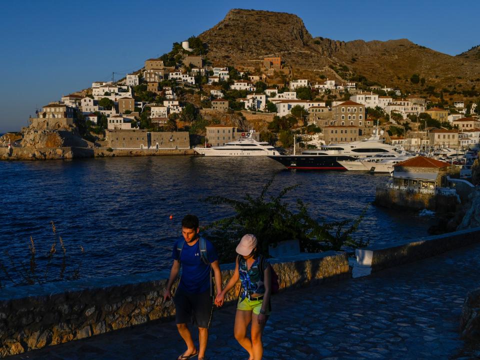 A couple walks hand in hand past the harbour in Hydra, a Greek island.