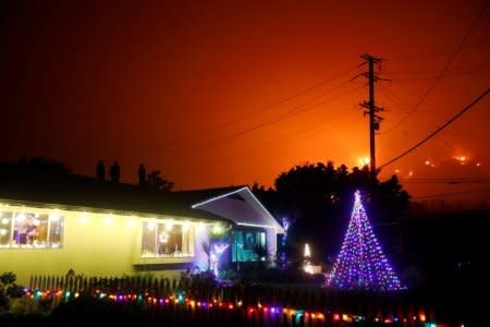 People stand on a roof of a home illuminated with Christmas lights to watch wildfire on a hillside burn during the Thomas Fire in Santa Barbara county near Carpinteria, California, U.S. December 11, 2017. REUTERS/Patrick T Fallon