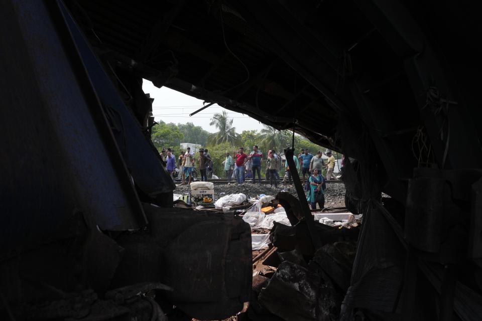 People watch the wreckage of passenger trains that derailed in Balasore district, in the eastern Indian state of Orissa, Saturday, June 3, 2023. Rescuers are wading through piles of debris and wreckage to pull out bodies and free people after two passenger trains derailed in India, killing more than 280 people and injuring hundreds as rail cars were flipped over and mangled in one of the country’s deadliest train crashes in decades. (AP Photo/Rafiq Maqbool)