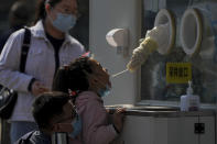 A man wearing a face mask helps a child to get her routine COVID-19 throat swab at a coronavirus testing site in Beijing, Thursday, Oct. 6, 2022. Sprawling Xinjiang is the latest Chinese region to be hit with sweeping COVID-19 travel restrictions, as China further ratchets up control measures ahead of a key Communist Party congress later this month. (AP Photo/Andy Wong)